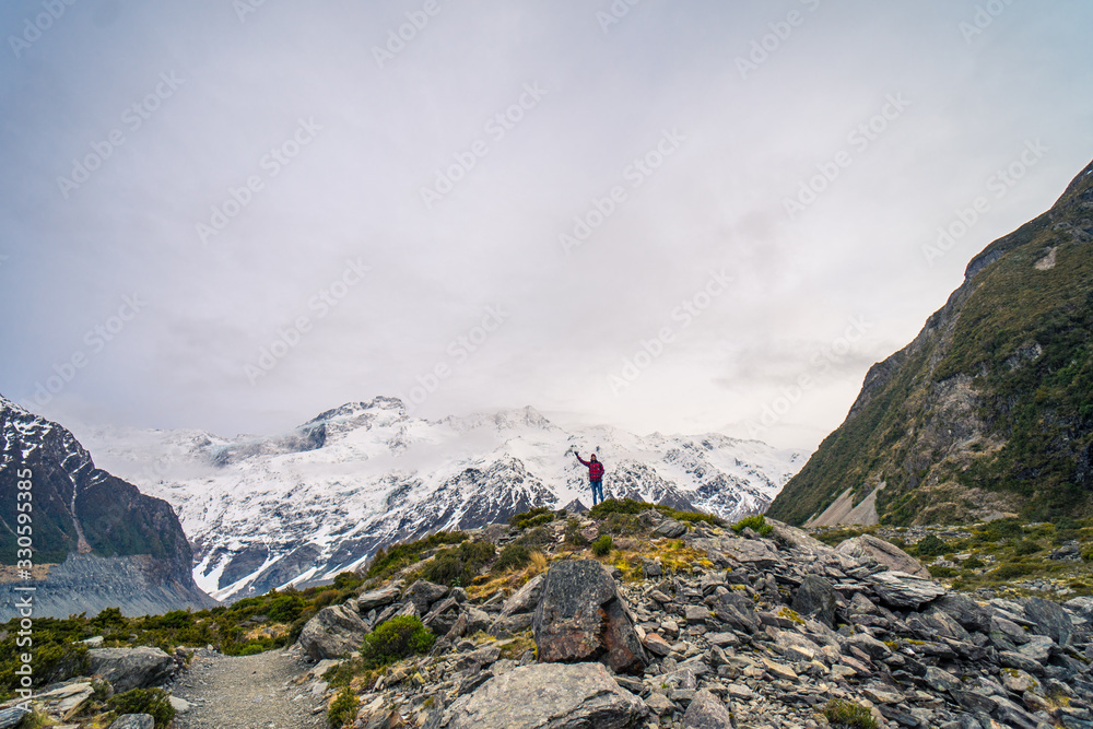 European man waving with snowy mountains in background at Hooker Valley Track, New Zealand