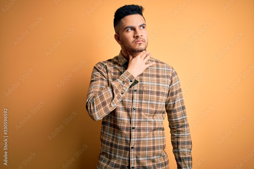 Young handsome man wearing casual shirt standing over isolated yellow background Touching painful neck, sore throat for flu, clod and infection Young handsome man wearing casual shirt standing over isolated yellow background Touching painful neck, sore throat for flu, clod and infection