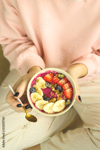 Smoothie bowl with banana, strawberries and blueberries and granola in female hands. Spring healthy breakfast concept.