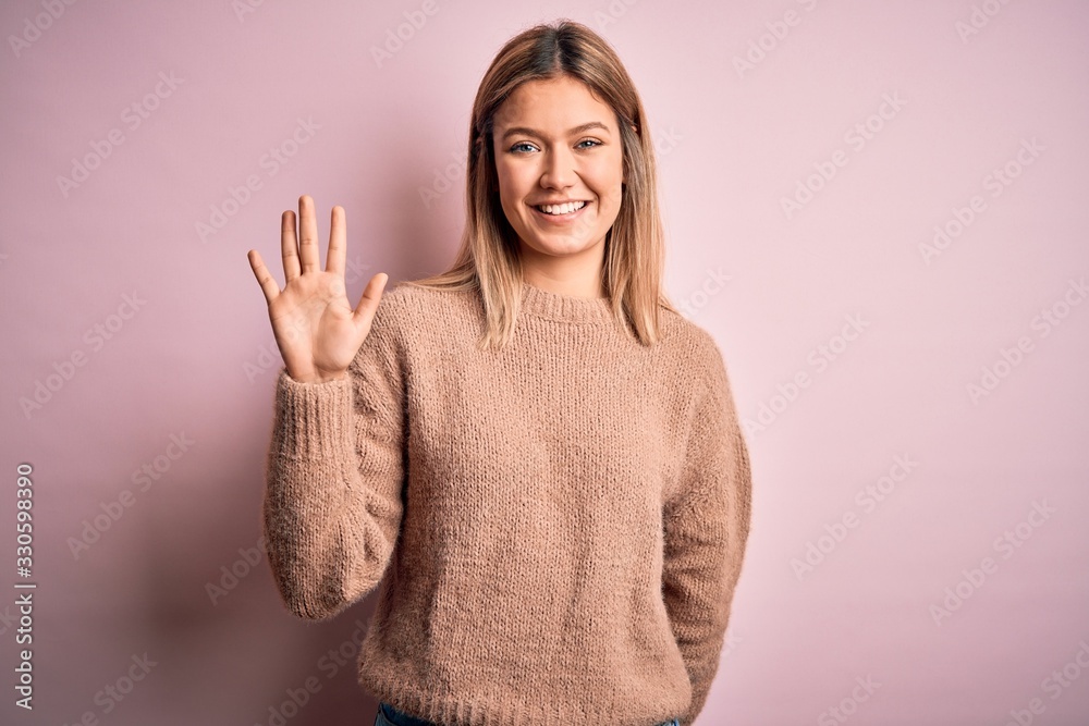 Young beautiful blonde woman wearing winter wool sweater over pink isolated background showing and pointing up with fingers number five while smiling confident and happy. Young beautiful blonde woman wearing winter wool sweater over pink isolated background showing and pointing up with fingers number five while smiling confident and happy.