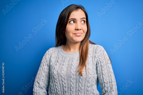 Beautiful young woman wearing casual wool sweater standing over blue isolated background smiling looking to the side and staring away thinking.