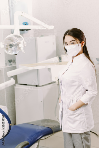 Fototapeta Naklejka Na Ścianę i Meble -  Cheerful female dentist smiling at her office. Beautiful woman student in a protective mask in dentistry stands in the dental office