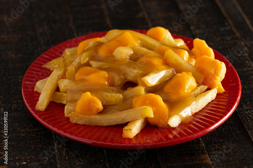 Plate of Poutine with Orange Cheddar Cheese with Brown Gravy on French Fries