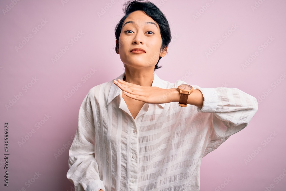 Young beautiful asian girl wearing casual shirt standing over isolated pink background cutting throat with hand as knife, threaten aggression with furious violence Young beautiful asian girl wearing casual shirt standing over isolated pink background cutting throat with hand as knife, threaten aggression with furious violence