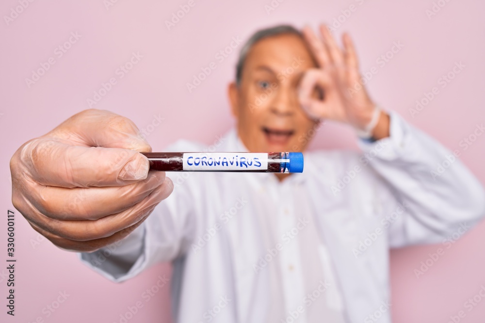 Senior handsome hoary man holding coronavirus tube test over isolated pink background with happy face smiling doing ok sign with hand on eye looking through fingers Senior handsome hoary man holding coronavirus tube test over isolated pink background with happy face smiling doing ok sign with hand on eye looking through fingers