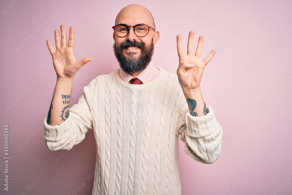 Φωτογραφία Handsome bald man with beard and tattoo wearing glasses and sweater over pink background showing and pointing up with fingers number nine while smiling confident and happy