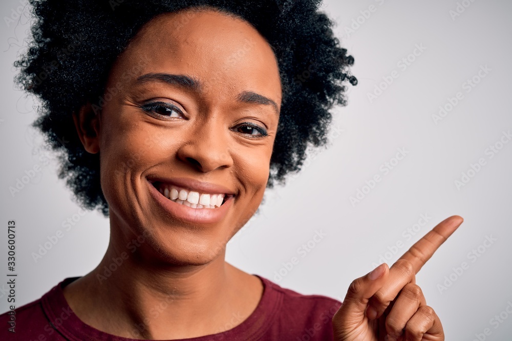 Young beautiful African American afro woman with curly hair standing over white background very happy pointing with hand and finger to the side Young beautiful African American afro woman with curly hair standing over white background very happy pointing with hand and finger to the side