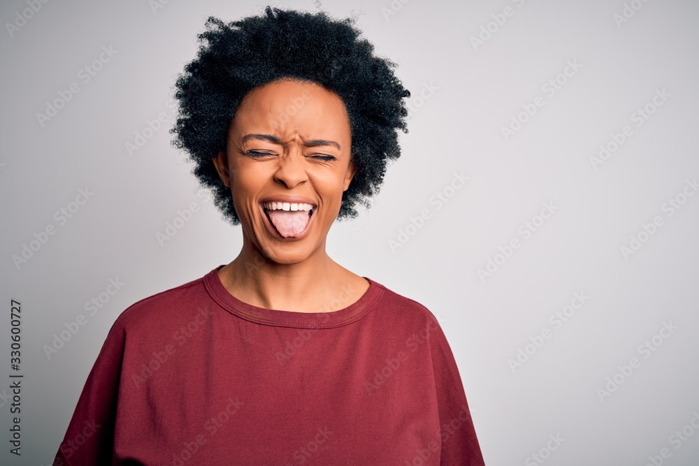 Young beautiful African American afro woman with curly hair wearing casual t-shirt standing sticking tongue out happy with funny expression. Emotion concept.