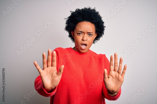 Young beautiful African American afro woman with curly hair wearing red casual sweater doing stop gesture with hands palms, angry and frustration expression