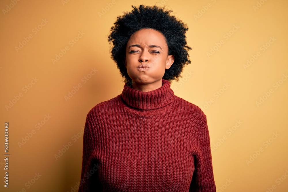 Young beautiful African American afro woman with curly hair wearing casual turtleneck sweater puffing cheeks with funny face. Mouth inflated with air, crazy expression. Young beautiful African American afro woman with curly hair wearing casual turtleneck sweater puffing cheeks with funny face. Mouth inflated with air, crazy expression.