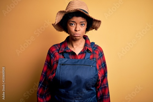 Young African American afro farmer woman with curly hair wearing apron and hat depressed and worry for distress, crying angry and afraid. Sad expression.