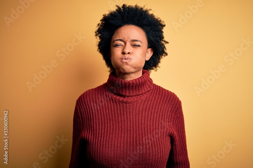 Young beautiful African American afro woman with curly hair wearing casual turtleneck sweater puffing cheeks with funny face. Mouth inflated with air, crazy expression. © Krakenimages.com