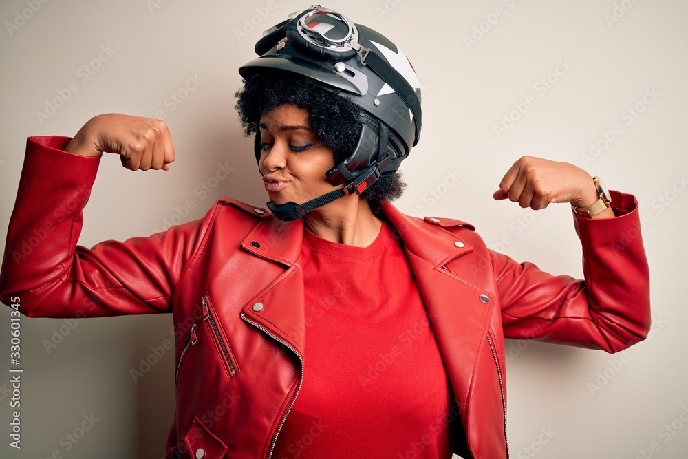 Young African American afro motorcyclist woman with curly hair wearing motorcycle helmet showing arms muscles smiling proud. Fitness concept. Young African American afro motorcyclist woman with curly hair wearing motorcycle helmet showing arms muscles smiling proud. Fitness concept.