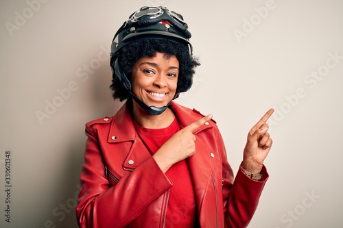 Young African American afro motorcyclist woman with curly hair wearing motorcycle helmet smiling and looking at the camera pointing with two hands and fingers to the side.