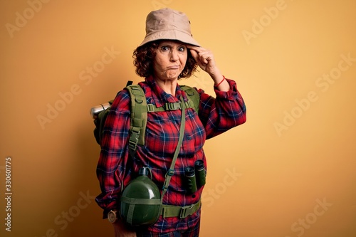Middle age curly hair hiker woman hiking wearing backpack and water canteen using binoculars worried and stressed about a problem with hand on forehead, nervous and anxious for crisis