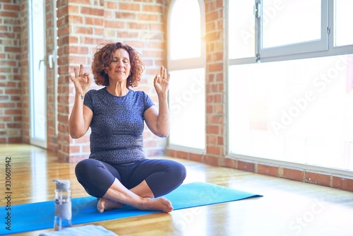 Middle age beautiful sportswoman wearing sportswear sitting on mat practicing yoga at home relax and smiling with eyes closed doing meditation gesture with fingers. Yoga concept.