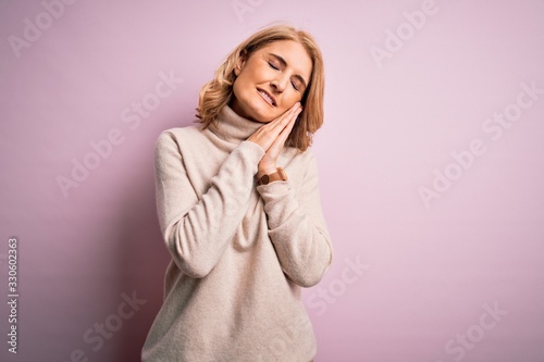 Middle age beautiful blonde woman wearing casual turtleneck sweater over pink background sleeping tired dreaming and posing with hands together while smiling with closed eyes. © Krakenimages.com