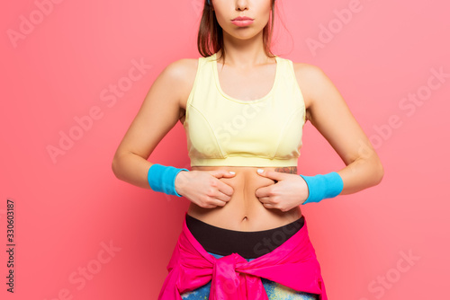 cropped view of displeased sportswoman touching her body on pink background