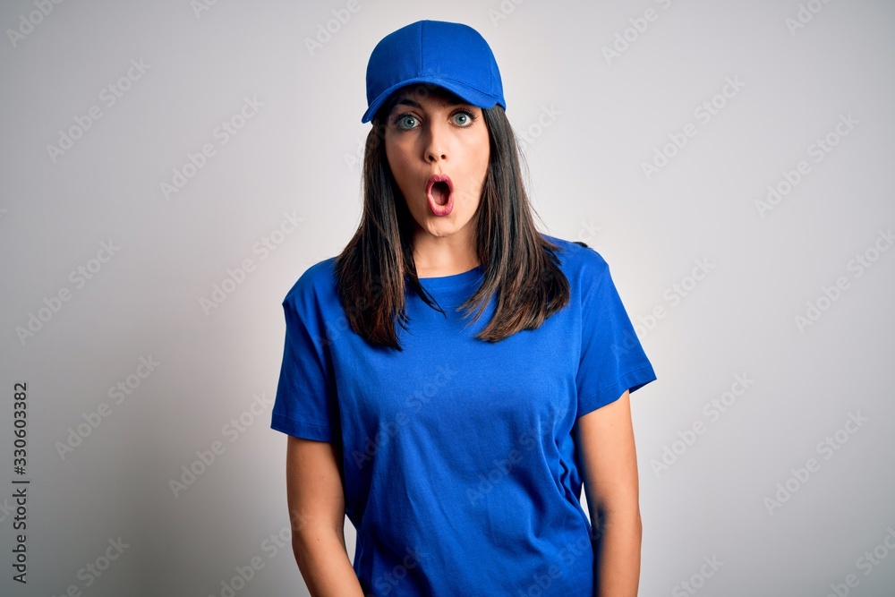 Young delivery woman with blue eyes wearing cap standing over blue background afraid and shocked with surprise expression, fear and excited face. Young delivery woman with blue eyes wearing cap standing over blue background afraid and shocked with surprise expression, fear and excited face.