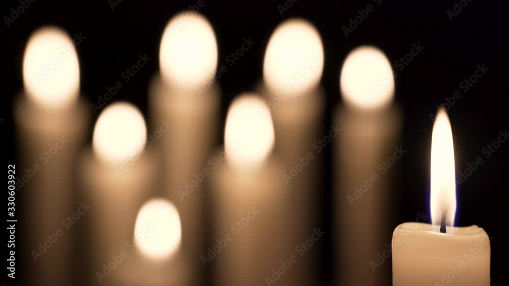 Close-up of a candle flame in the front and bokeh of other six candles in the background.