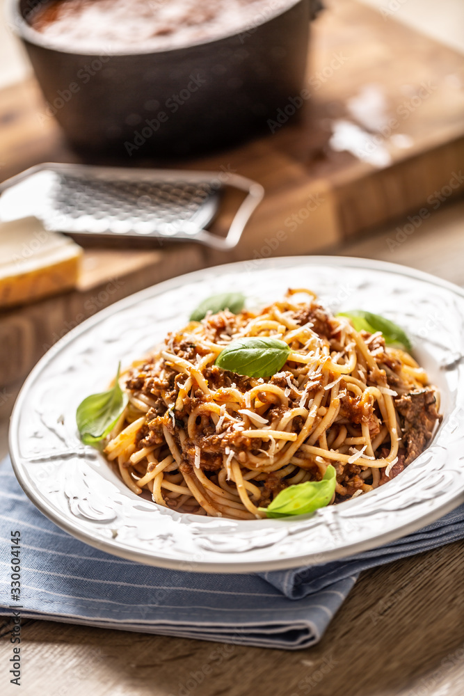 Italian pasta spaghetti bolognese served on white plate with parmesan cheese and basil