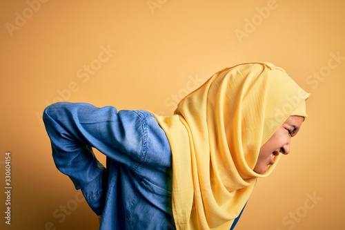 Young beautiful woman with curly hair wearing arab traditional hijab over yellow background Suffering of backache, touching back with hand, muscular pain