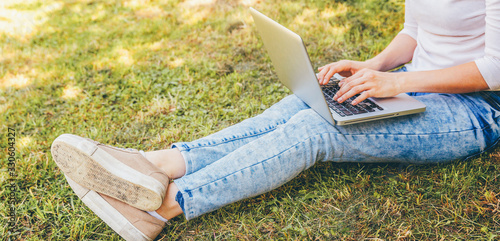Freelance business concept. Woman legs on green grass lawn in city park, hands working on laptop pc computer. Lifestyle authentic candid student girl studying outdoors. Mobile Office.