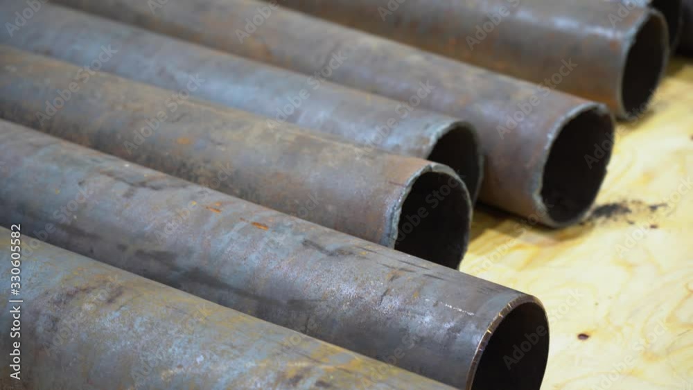 Long metal pipes with smooth sandededges lie on the floor, on sheet of plywood. The walls of the pipes are very thick. Close up view of stack round rusty iron tubes. Long metal pipes with smooth sandededges lie on the floor, on sheet of plywood. The walls of the pipes are very thick. Close up view of stack round rusty iron tubes.