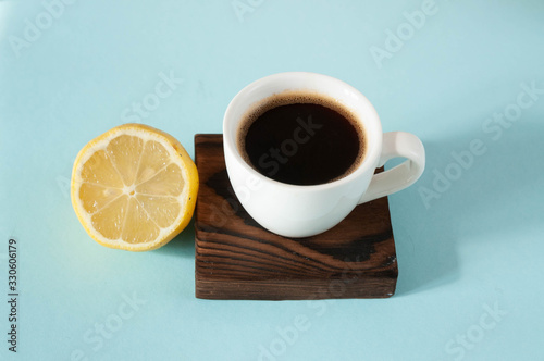 White little cup of coffee on burnt wood stand, with half of lemon on blue color background, organic coffee break, hipster style food