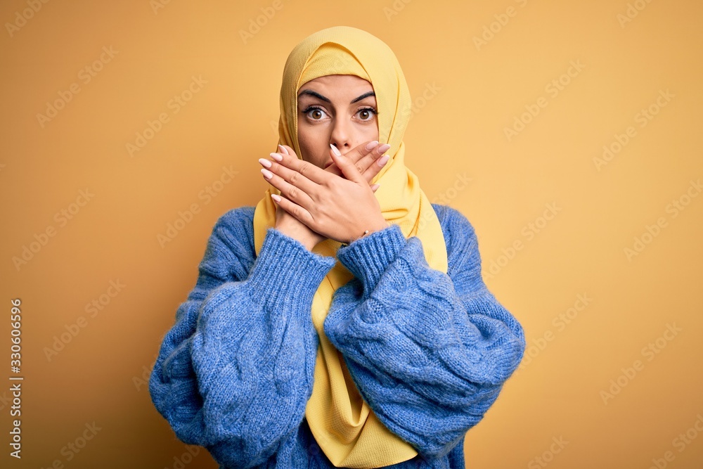 Young beautiful brunette muslim woman wearing arab hijab over isolated yellow background shocked covering mouth with hands for mistake. Secret concept. Young beautiful brunette muslim woman wearing arab hijab over isolated yellow background shocked covering mouth with hands for mistake. Secret concept.