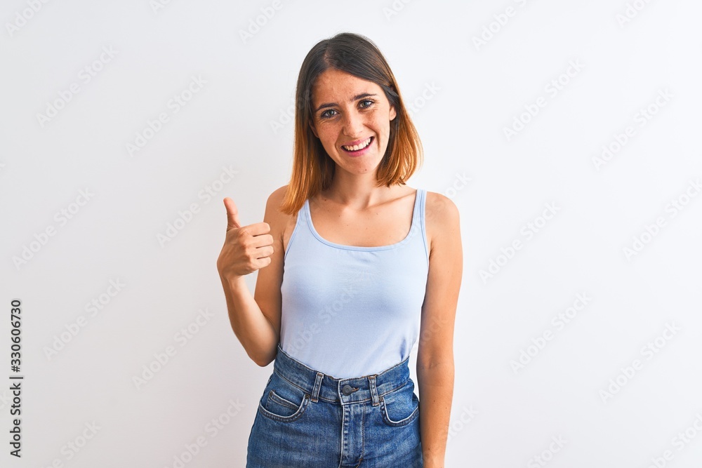 Beautiful redhead woman standing over isolated background doing happy thumbs up gesture with hand. Approving expression looking at the camera showing success. Beautiful redhead woman standing over isolated background doing happy thumbs up gesture with hand. Approving expression looking at the camera showing success.