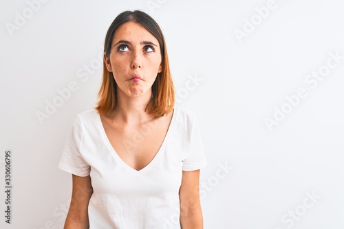 Beautiful redhead woman wearing casual white t-shirt over isolated background making fish face with lips, crazy and comical gesture. Funny expression. © Krakenimages.com