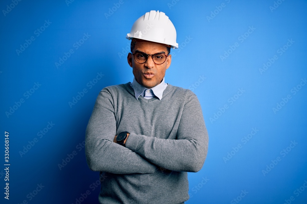 Young handsome african american engineer man with dreadlocks wearing safety helmet skeptic and nervous, disapproving expression on face with crossed arms. Negative person. Young handsome african american engineer man with dreadlocks wearing safety helmet skeptic and nervous, disapproving expression on face with crossed arms. Negative person.