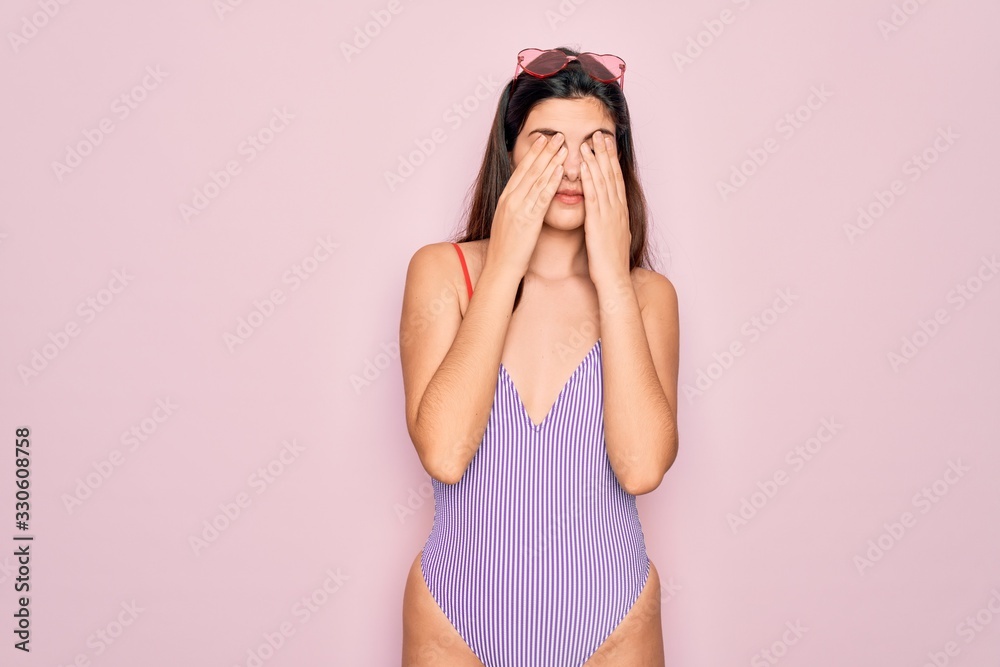 Young beautiful fashion girl wearing swimwear swimsuit and sunglasses over pink background rubbing eyes for fatigue and headache, sleepy and tired expression. Vision problem Young beautiful fashion girl wearing swimwear swimsuit and sunglasses over pink background rubbing eyes for fatigue and headache, sleepy and tired expression. Vision problem