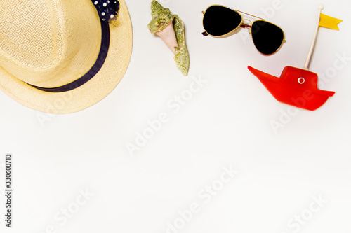 Sea, shells, sunglasses, toy boat, hat on a light background with sand, top view
