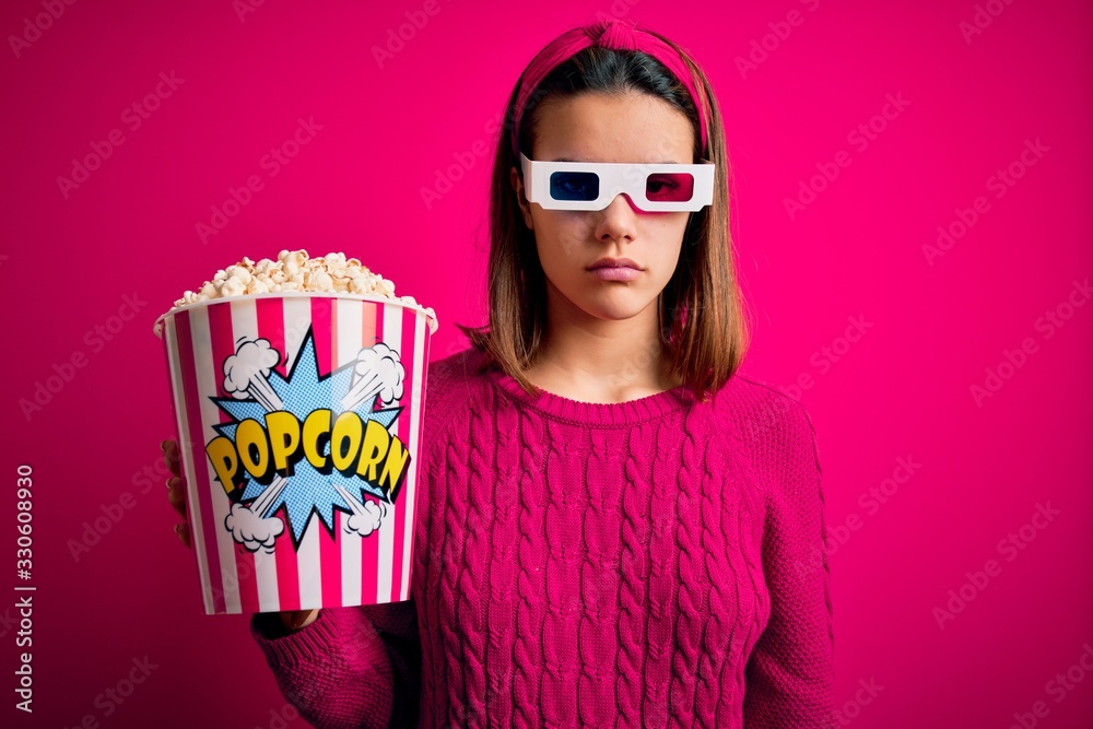 Obraz premium Young beautiful girl watching movie using 3d glasses eating box with popcorns skeptic and nervous, frowning upset because of problem. Negative person.