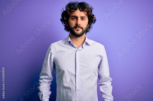 Young handsome business man with beard wearing shirt standing over purple background Relaxed with serious expression on face. Simple and natural looking at the camera. © Krakenimages.com