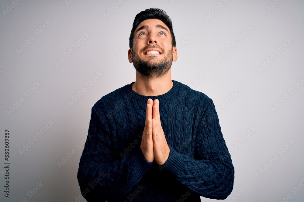Young handsome man with beard wearing casual sweater standing over white background begging and praying with hands together with hope expression on face very emotional and worried. Begging. Young handsome man with beard wearing casual sweater standing over white background begging and praying with hands together with hope expression on face very emotional and worried. Begging.