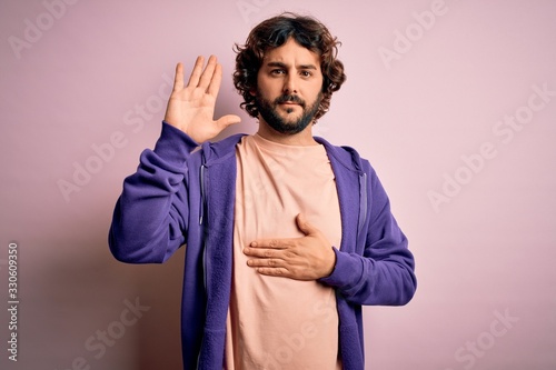 Young handsome sporty man with beard wearing casual sweatshirt over pink background Swearing with hand on chest and open palm, making a loyalty promise oath