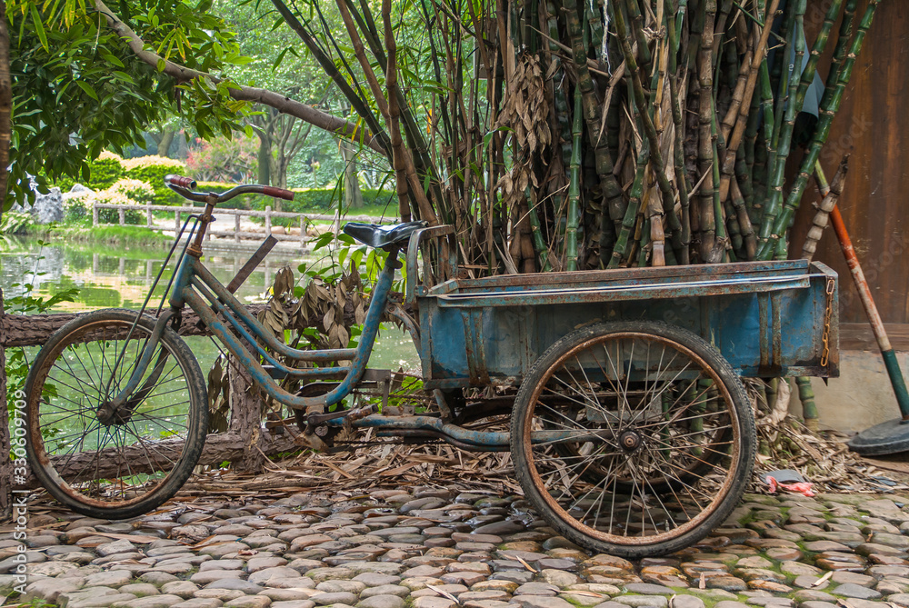 Guilin, China - May 11, 2010: Seven Star Park. Closeup of blue transport tricycle with pedals in front of green and brown garden scenery.