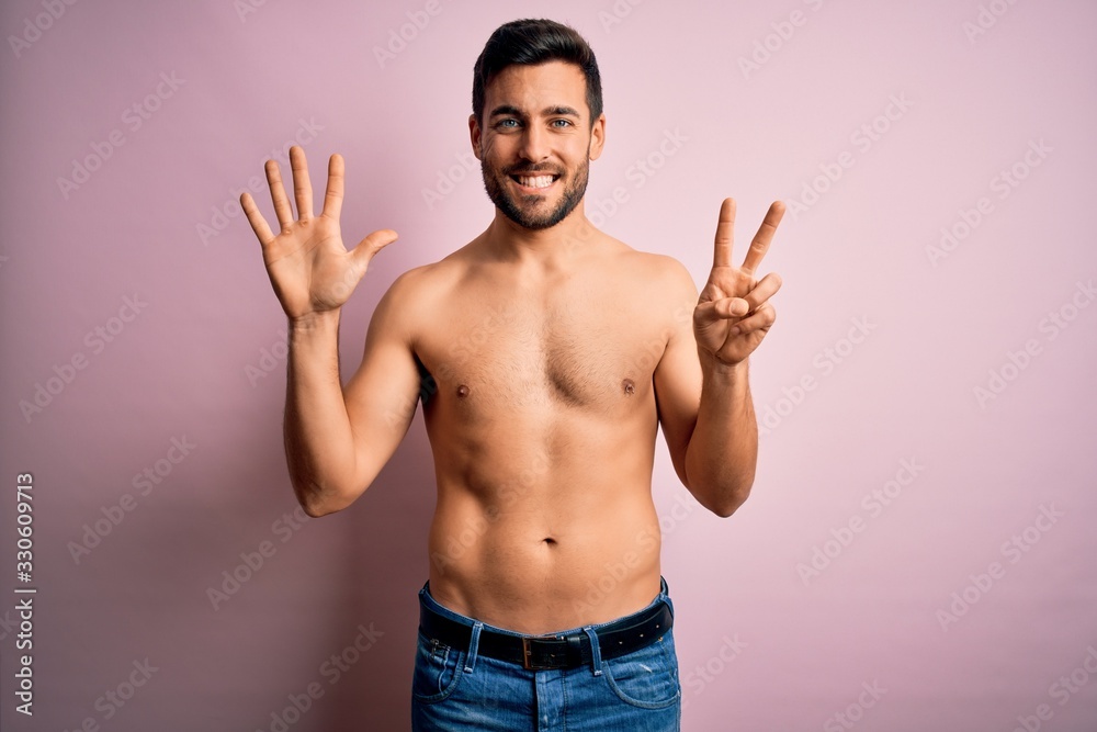 Young handsome strong man with beard shirtless standing over isolated pink background showing and pointing up with fingers number seven while smiling confident and happy.