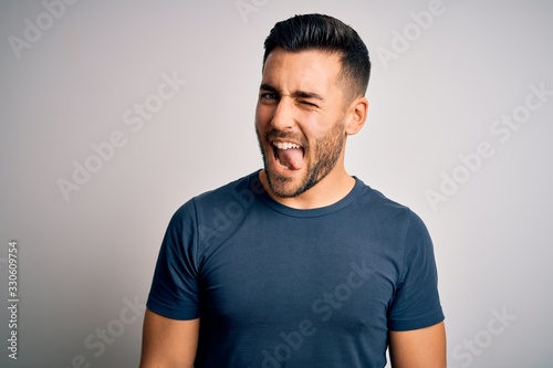 Young handsome man wearing casual t-shirt standing over isolated white background winking looking at the camera with sexy expression, cheerful and happy face.