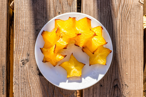 Closeup flat top view of sliced yellow starfruit on plate on wooden table background outside with vibrant color photo