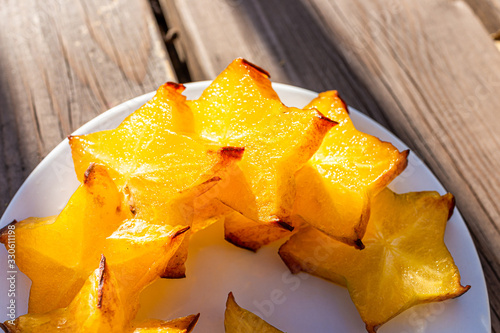 Closeup macro texture view of sliced yellow starfruit on plate on wooden table background outside with vibrant color photo