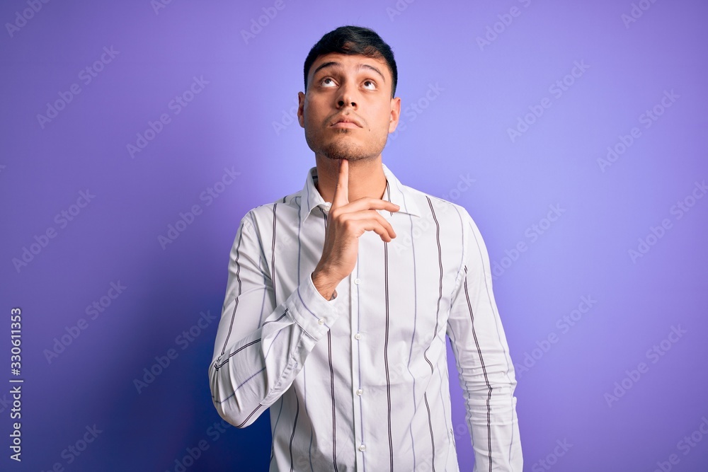Young handsome hispanic man wearing elegant business shirt standing over purple background Thinking concentrated about doubt with finger on chin and looking up wondering Young handsome hispanic man wearing elegant business shirt standing over purple background Thinking concentrated about doubt with finger on chin and looking up wondering