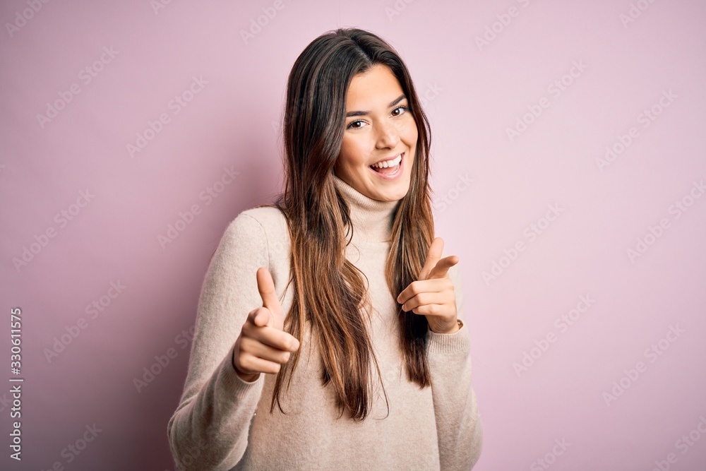 Young beautiful girl wearing casual turtleneck sweater standing over isolated pink background pointing fingers to camera with happy and funny face. Good energy and vibes. Young beautiful girl wearing casual turtleneck sweater standing over isolated pink background pointing fingers to camera with happy and funny face. Good energy and vibes.