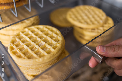 Closeup macro of hand opening waffles on bakery tray buffet for morning continental breakfast in hotel motel or office