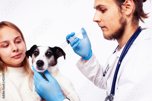 young veterinarian doctor in blue gloves examine little cute dog jack russell isolated on white background with owner blond girl holding it, animal healthcare