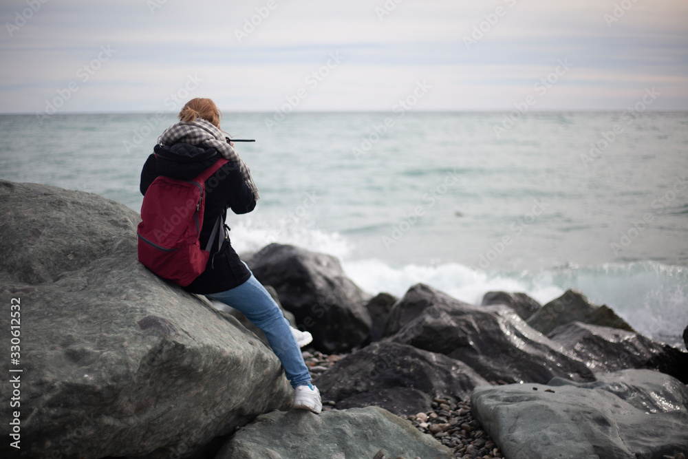 A girl sits on a stone by the sea.