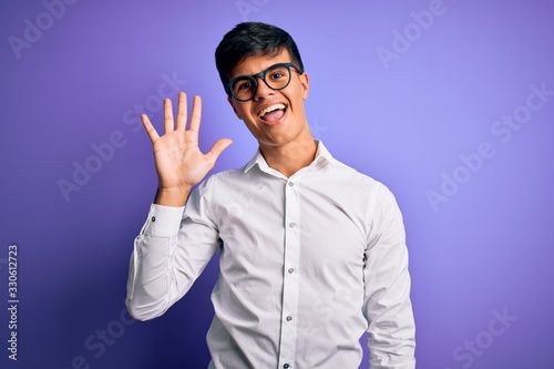 Young handsome business man wearing shirt and glasses over isolated purple background showing and pointing up with fingers number five while smiling confident and happy.